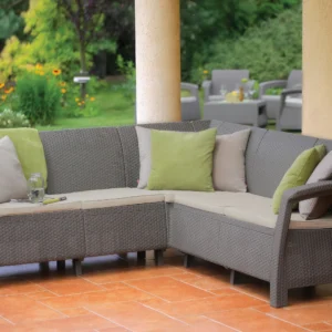 Zdjęcie narożnika ogrodowego CORFU RELAX Cappuccino, wykonanego z tworzywa sztucznego imitującego rattan, z jasnymi poduszkami na siedziska i ozdobnymi poduszkami na oparciach.