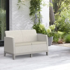 Sofa ogrodowa Keter Scandi Forma 2 w kolorze Pebble Grey-Soft Beige Oat stoi na drewnianym tarasie pośród zieleni