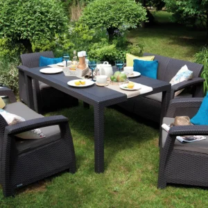 Zestaw ogrodowy CORFU FIESTA II Graphite – grafitowy stół prostokątny otoczony dwiema kanapami i dwoma fotelami z technorattanu, na trawniku, ozdobiony kolorowymi poduszkami i śnia Zestaw ogrodowy CORFU FIESTA II Graphite – grafitowy stół prostokątny otoczony dwiema kanapami i dwoma fotelami z technorattanu, na trawniku, ozdobiony kolorowymi poduszkami i śnia