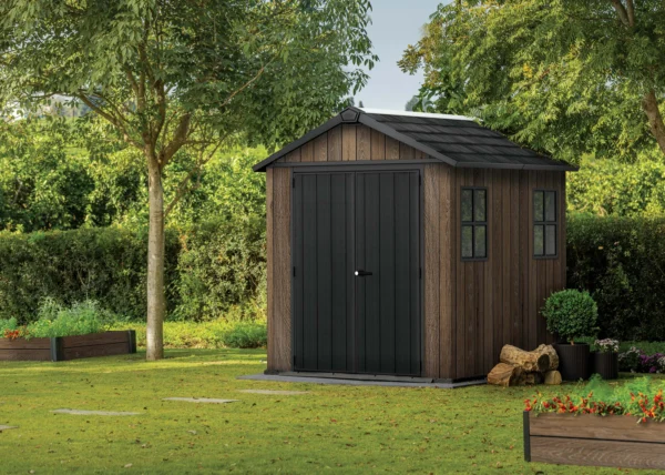 Domek narzędziowy Keter DECO APEX 757/775 w kolorze orzecha włoskiego z czarnymi drzwiami i oknami w ogrodzie Domek narzędziowy Keter DECO APEX 757/775 w kolorze orzecha włoskiego z czarnymi drzwiami i oknami w ogrodzie